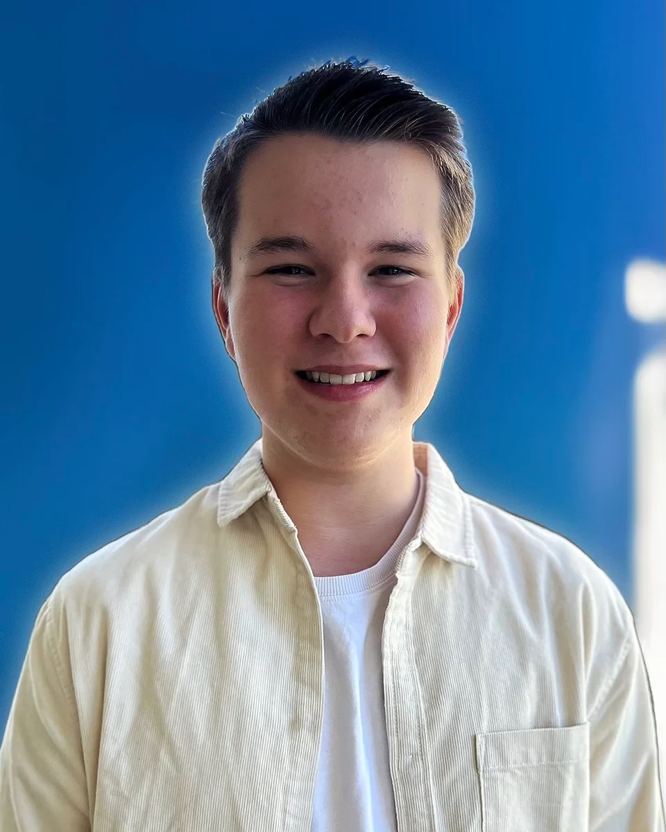 Noah Moller, smiling, in a cream corduroy shirt against a blue wall.